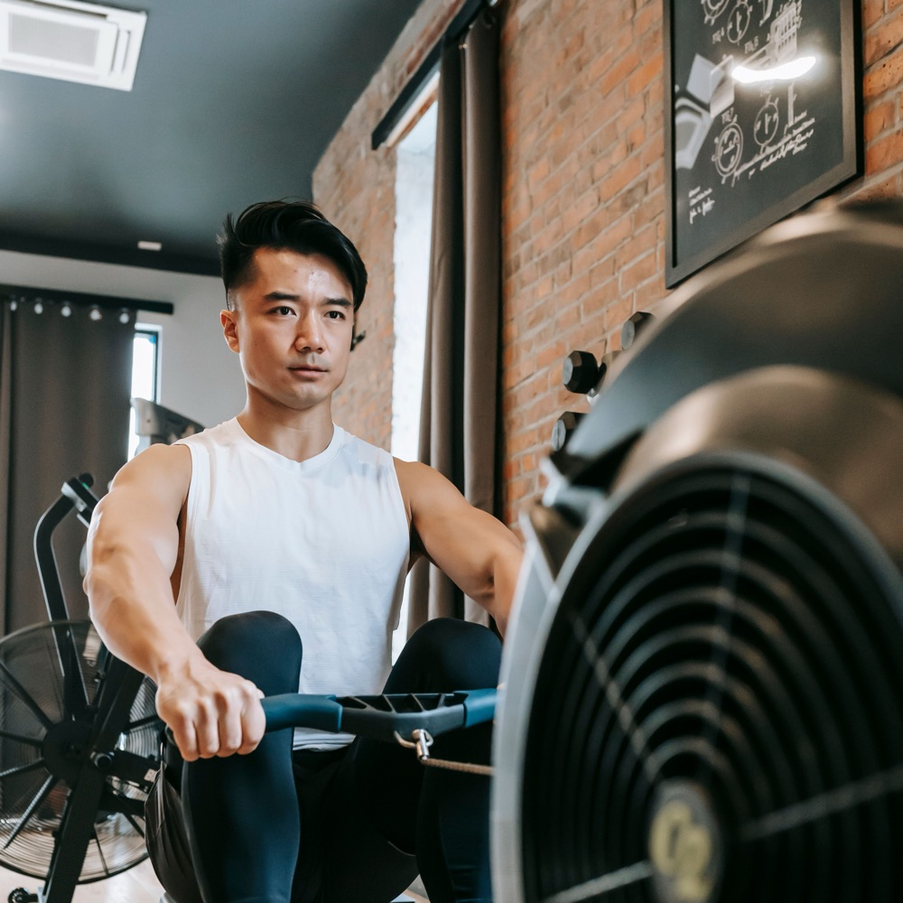 A man pulling hard on a rowing machine, the effort showing on his face.